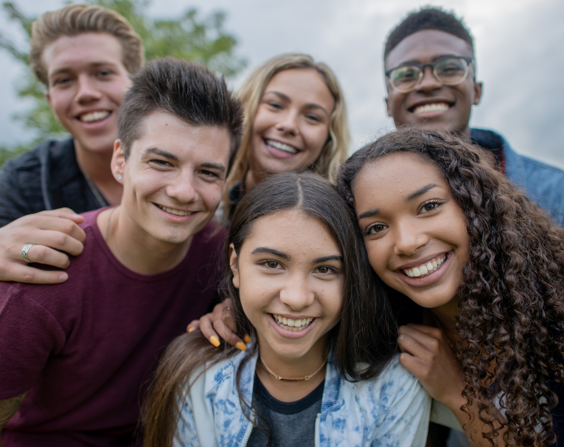 Mixed race teenagers taking a selfie in a crowd outside.